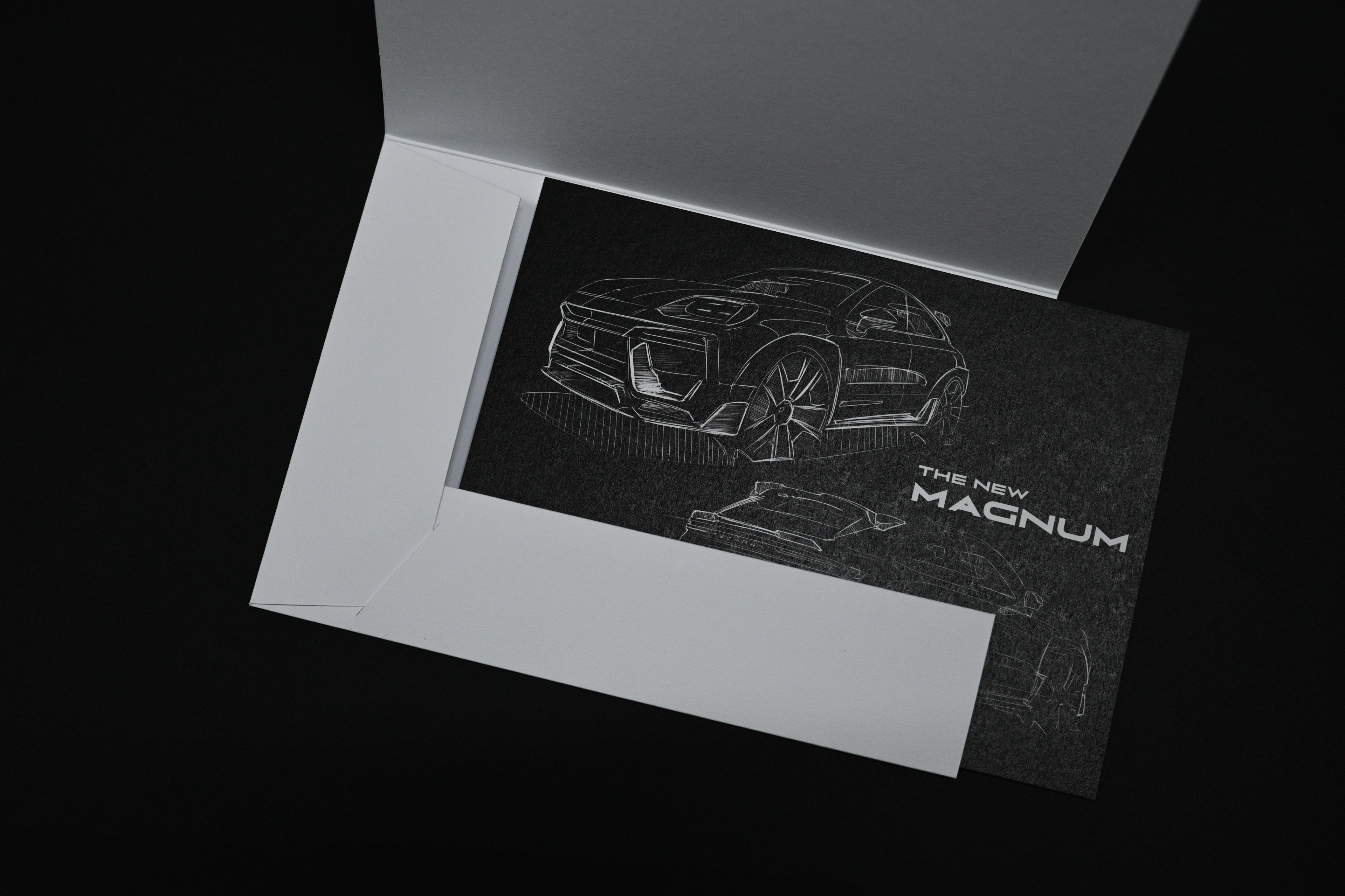 Schwarze Karte mit weißer Skizze eines Autos und dem Text „THE NEW MAGNUM“, teilweise in einen weißen Umschlag auf schwarzem Hintergrund eingelegt.